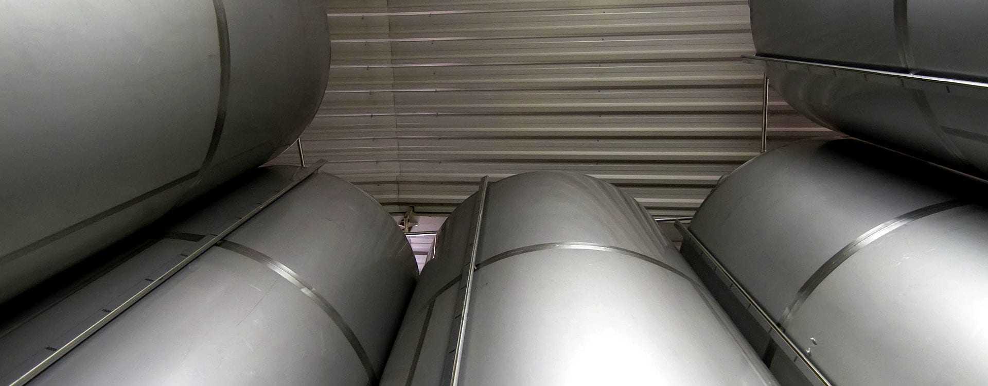Stacked metal storage tanks in a warehouse with a metallic finish and cylindrical shape. - Olive Oil Times