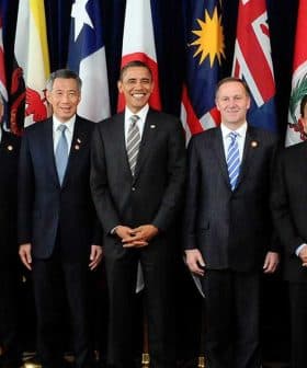 Group of ten political leaders posing for a photo at an international summit with flags in the background. - Olive Oil Times