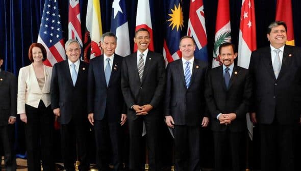 Group of ten political leaders posing for a photo at an international summit with flags in the background. - Olive Oil Times