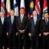 Group of ten political leaders posing for a photo at an international summit with flags in the background. - Olive Oil Times