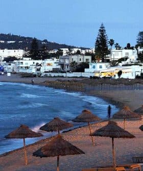 Coastal view featuring beach umbrellas and white buildings along the shoreline at dusk. - Olive Oil Times