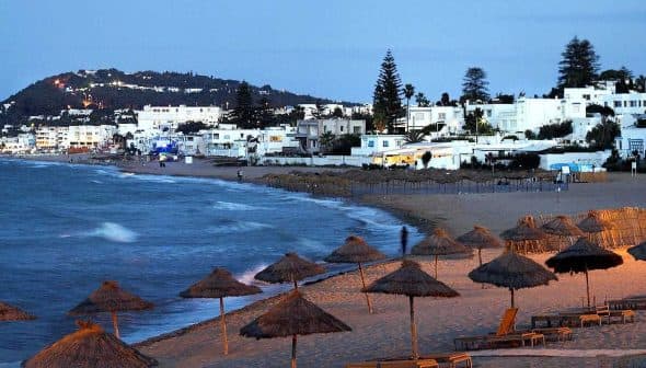 Coastal view featuring beach umbrellas and white buildings along the shoreline at dusk. - Olive Oil Times