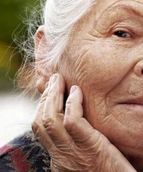 Elderly woman with gray hair and a thoughtful expression, resting her chin on her hand. - Olive Oil Times