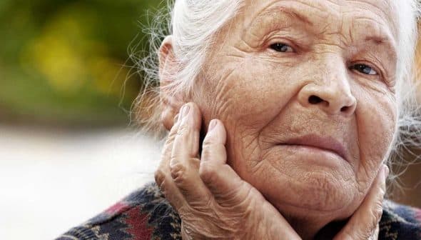 Elderly woman with gray hair and a thoughtful expression, resting her chin on her hand. - Olive Oil Times