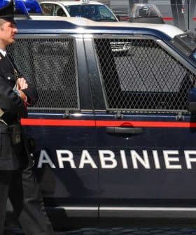 A Carabinieri officer standing next to a marked police vehicle in an urban setting. - Olive Oil Times