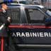 A Carabinieri officer standing next to a marked police vehicle in an urban setting. - Olive Oil Times
