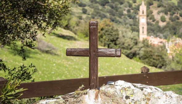 A wooden cross placed on a rock in a natural outdoor setting with greenery in the background. - Olive Oil Times