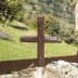 A wooden cross placed on a rock in a natural outdoor setting with greenery in the background. - Olive Oil Times