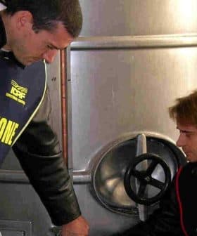 Two inspectors in vests examining olive oil storage tanks in a facility. - Olive Oil Times