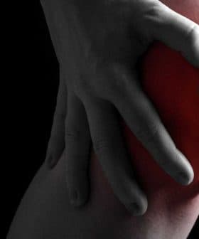 Individual holding their knee with both hands, indicating discomfort or pain in the knee area. - Olive Oil Times