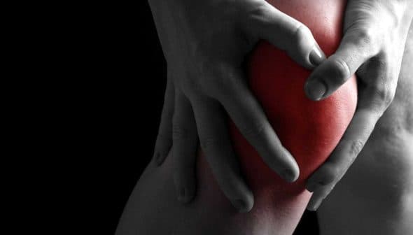 Individual holding their knee with both hands, indicating discomfort or pain in the knee area. - Olive Oil Times