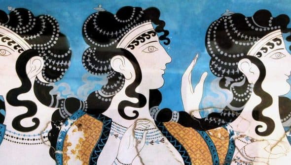 Ancient fresco showing three women with elaborate hairstyles and decorative clothing against a blue background. - Olive Oil Times