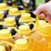 A hand gripping a bottle of oil with a yellow cap among multiple bottles on a shelf. - Olive Oil Times