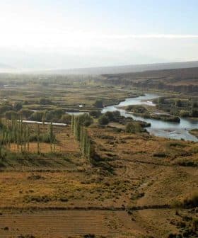 Aerial view of a landscape featuring a river, greenery, and mountains in the background. - Olive Oil Times