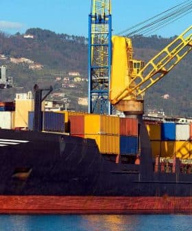 Cargo ship docked at a port with various colorful shipping containers stacked on board. - Olive Oil Times