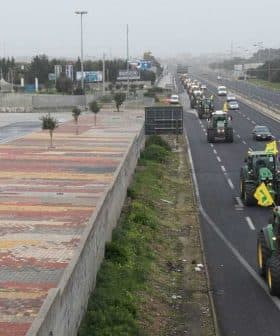 Multiple tractors driving on a highway with vehicles in the background. - Olive Oil Times