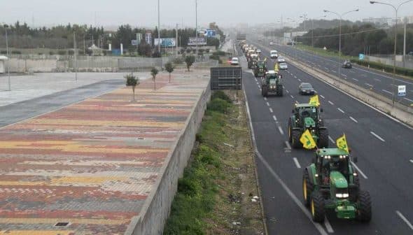 Multiple tractors driving on a highway with vehicles in the background. - Olive Oil Times