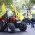 Red tractor surrounded by yellow flags at a demonstration in an urban area. - Olive Oil Times