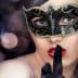 Woman with a black masquerade mask and finger on lips, signaling silence. - Olive Oil Times