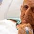 Elderly man lying in a hospital bed with an intravenous line in his hand. - Olive Oil Times