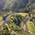 Aerial view of a winding river surrounded by olive trees in a hilly landscape. - Olive Oil Times