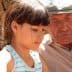 A young girl and an elderly man sitting together, focused on an activity outdoors. - Olive Oil Times