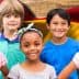 Five children posing together in front of a Spanish flag background, smiling and wearing casual clothing. - Olive Oil Times