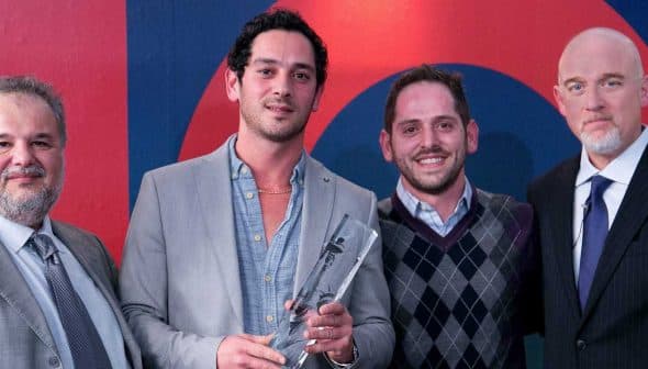 Four men standing together, one holding an award, in a formal setting with a colorful background. - Olive Oil Times