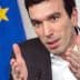 Man in a suit gesturing with hands during a discussion, European Union flag visible in the background. - Olive Oil Times