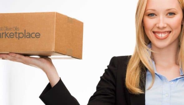 A woman in a black blazer holding a cardboard package with marketplace branding. - Olive Oil Times