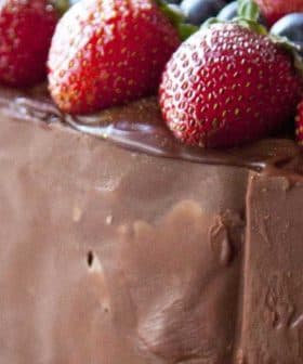 Chocolate cake topped with strawberries and blueberries, surrounded by rose petals. - Olive Oil Times