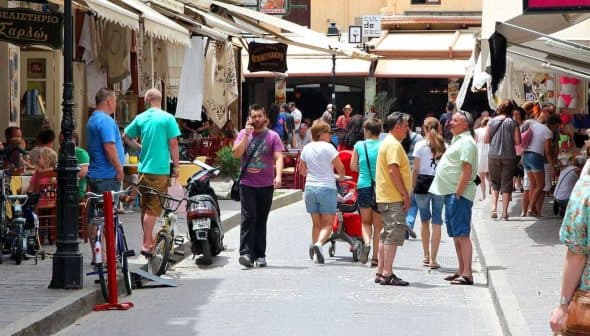 People walking and shopping in a market street with various shops and stalls. - Olive Oil Times