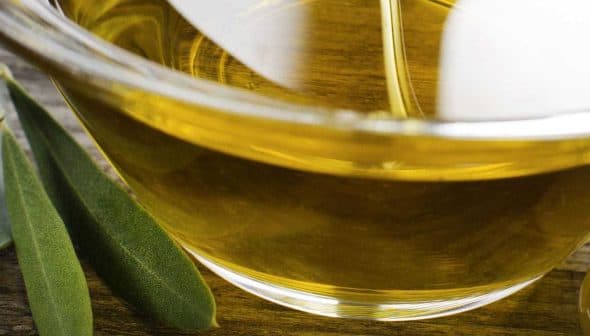 Close-up of a glass bowl filled with olive oil, surrounded by olives and olive leaves. - Olive Oil Times