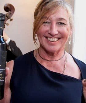 Woman in a navy dress holding a bottle of wine and a tall glass at an indoor event. - Olive Oil Times