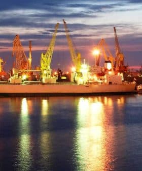 Cargo ships docked at a port with cranes illuminated by lights during twilight hours. - Olive Oil Times