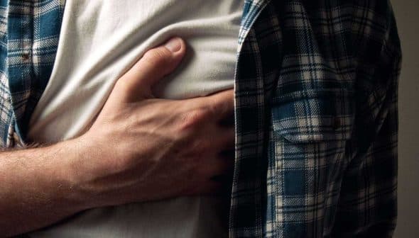 Individual in a plaid shirt holding their chest with a pained expression. - Olive Oil Times