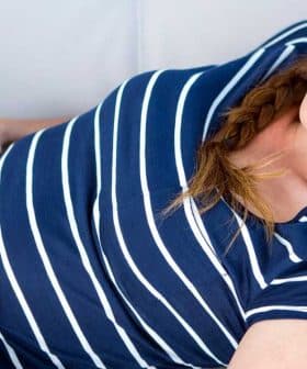 Pregnant woman in a striped shirt lying on a couch with a pained expression, holding her stomach. - Olive Oil Times