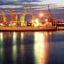 Cargo ships docked at a port with cranes illuminated at twilight. - Olive Oil Times