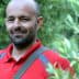 Man wearing a red polo shirt standing among olive trees with a slight smile. - Olive Oil Times