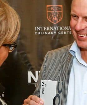 A man smiling while receiving an award from a woman at a culinary event. - Olive Oil Times