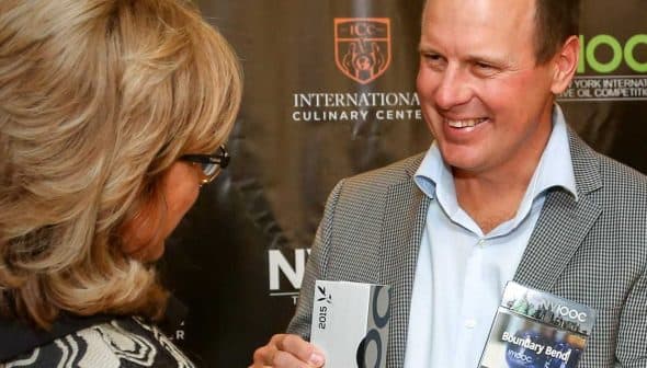 A man smiling while receiving an award from a woman at a culinary event. - Olive Oil Times