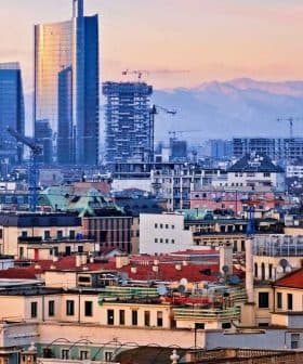 Panoramic view of Milan featuring modern skyscrapers and traditional buildings under a sunset sky. - Olive Oil Times