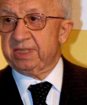 Elderly man wearing glasses and a dark suit speaking during an event. - Olive Oil Times