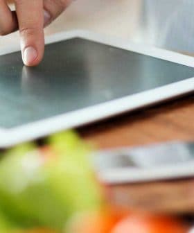 A person pointing at a tablet screen while preparing food in a kitchen setting. - Olive Oil Times