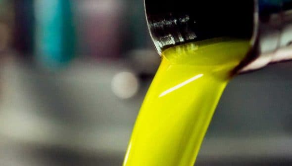 Stream of bright yellow olive oil pouring from a metal container into a bowl. - Olive Oil Times