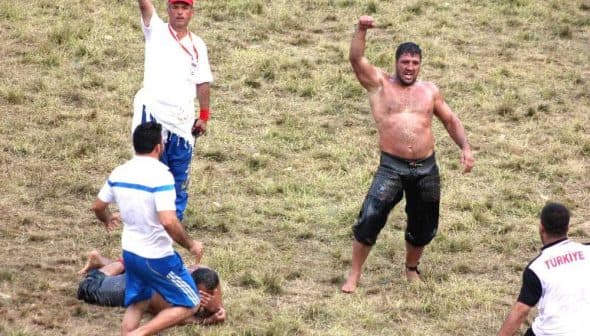 Competitors in a Turkish oil wrestling match with one wrestler celebrating a victory in a grassy field. - Olive Oil Times