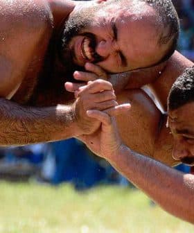Two male wrestlers in a Greco-Roman wrestling match, grappling on a grassy field. - Olive Oil Times