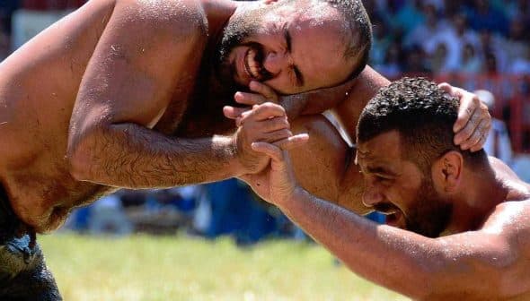 Two male wrestlers in a Greco-Roman wrestling match, grappling on a grassy field. - Olive Oil Times