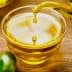A glass bowl filled with olive oil with a stream pouring from a vessel and olives nearby. - Olive Oil Times
