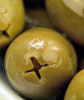 Close-up of green olives in a white bowl with a glossy surface. - Olive Oil Times